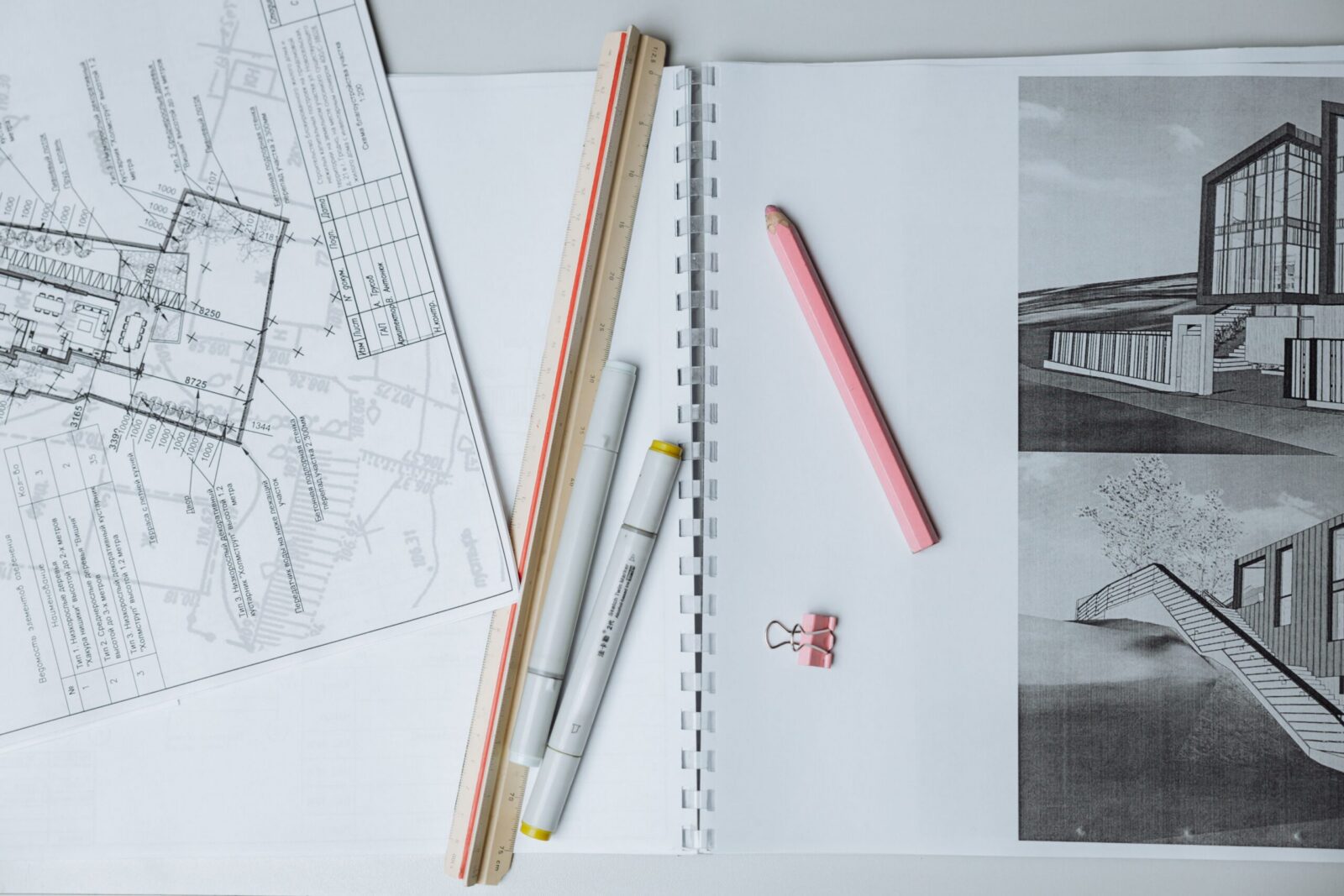 Flat lay of architectural blueprints, drawing tools, and stationery on a desk surface.